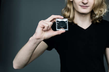 The guy holds a condom in his hand on a gray background.の写真素材