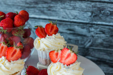 cupcake in the center with white cream decorated with ripe strawberries on a gray blue background...