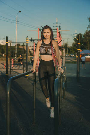 A young woman of athletic physique is doing an exercise on the uneven bars.