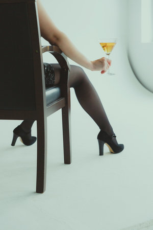 A woman in a chair sits with her back to the camera and holds a martini glass against the background of the window.の写真素材