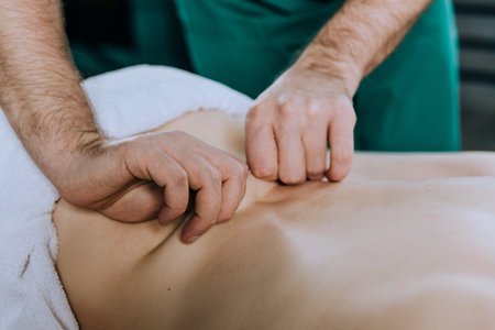 A man massage therapist in glasses and a green uniform massages the back of a woman.