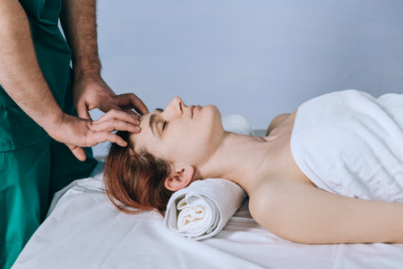 Face massage. Male hands make head massage to a beautiful young woman. Close-up of a woman getting spa treatment.の写真素材