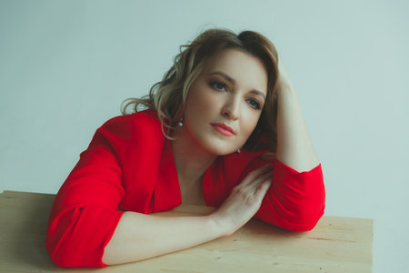 Beautiful blonde girl in a red jacket looks thoughtfully into the distance on gray background.の写真素材