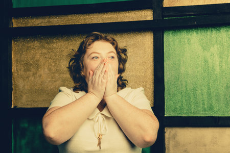 Red-haired plump woman covered her mouth with her hands in fright on a yellow background.の写真素材