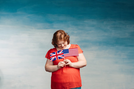 Red-haired plump woman holding British and American flags in front of him on a blue background.の写真素材