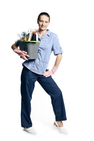 Attractive young woman in cleaning uniform and rubber gloves holding a bucket of cleaning products in her hands, isolated on white background.の写真素材