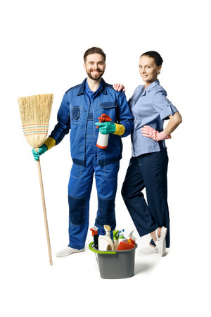 Attractive young woman and man in cleaning uniform and rubber gloves holding a broom cleaning products in his hands, isolated on white background.の写真素材