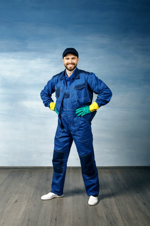 Thumb up. Young handsome man with a beard in a blue working uniform for cleaning rooms smiles isolated on blue background, thumbs up.の写真素材