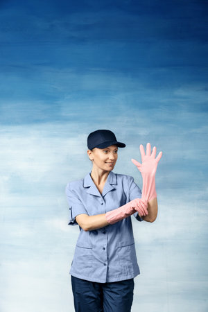 A beautiful young woman in the uniform of a maid and a baseball cap smiling and pulls on the glove on a blue background.の写真素材