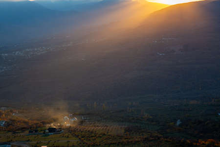The rays of the setting sun illuminate the mountain valley from under blue clouds.の写真素材
