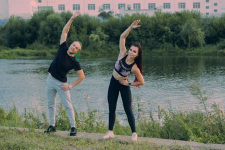 A man and a woman with interesting hairstyles (mohawk and braids) in sportswear doing stretching on...