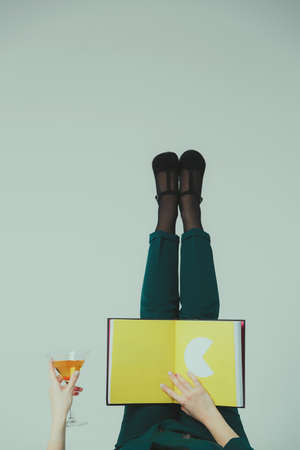 Female hands are holding an open book and Martini glass.の写真素材