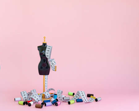 A scaled-down mannequin on a pink background with a tape for measuring and multicolored threads in...