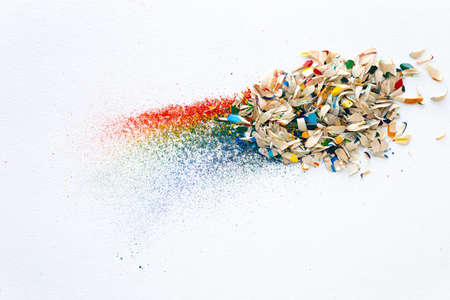 Shavings after sharpening of colored pencils lie in a heap on a white background. View from above
