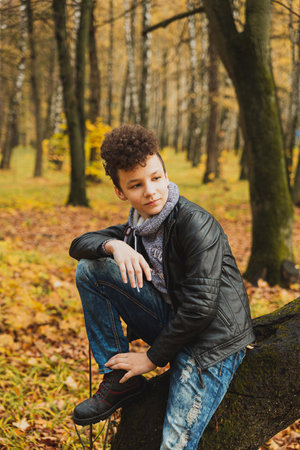 Curly brown-haired boy with a mohawk hairstyle in a leather jacket on an autumn background.の写真素材