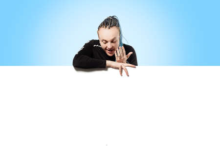 A man with an interesting hairstyle peers out from above a white poster and covers his mouth with his hand in surpriseの写真素材