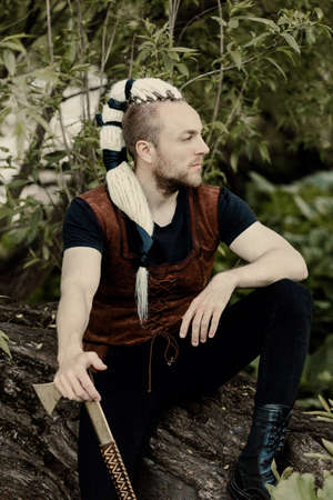 A young man with an interesting depicts a Viking with an ax in an unreliable stylized modern costume...