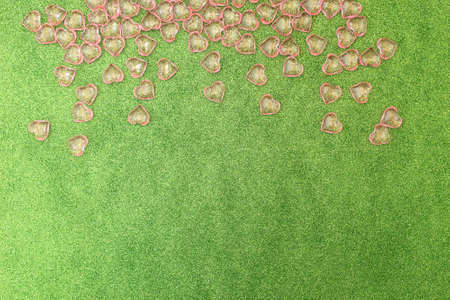 Pink transparent plastic hearts on green glittering background