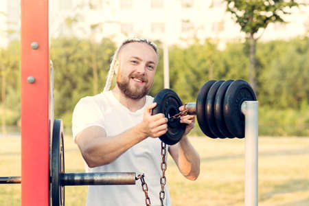 A man with a beard and braid hair prepares for a barbell press and lifts discs with weights.