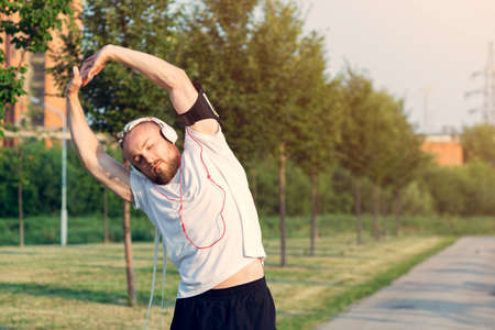 In the morning at sunrise, a man with an interesting braid hairstyle in headphones stretches before...