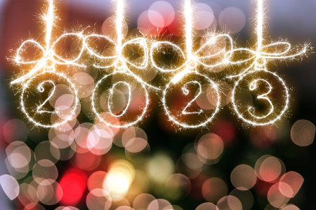 Christmas balls made of sparklers and the inscription 2023 on a red blurred background of New Years...