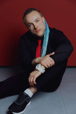 Young attractive man with an interesting haircut in braids on an undercut with a red tie on a red...