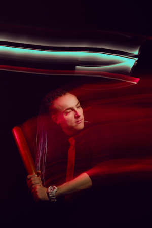 Handsome man with interesting braids on a black background with a baseball bat, shot with mixed...
