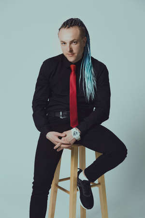 Young attractive man with an interesting haircut in braids on an undercut with a red tie on a light background.の写真素材