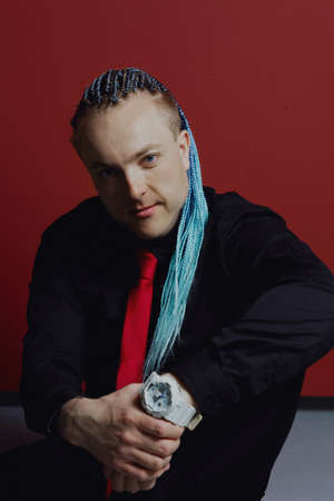 Young attractive man with an interesting haircut in braids on an undercut with a red tie on a red background.の写真素材