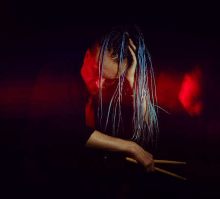 Handsome man with interesting braids on a black background with drumsticks, shot with mixed light.