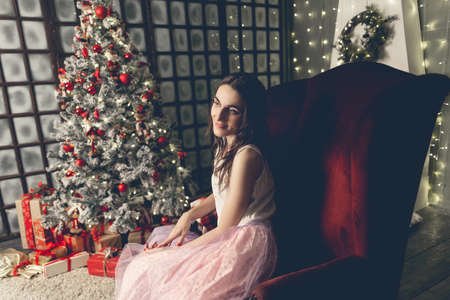 Beautiful young woman sits in a chair near the Christmas treeの写真素材