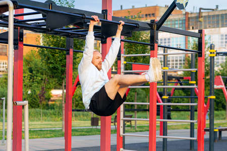 A man performs a leg raise on the bar in the morning on the sports field