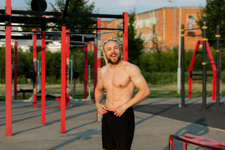 In the morning at sunrise, a man with an interesting braid hairstyle poses like a bodybuilder with a...
