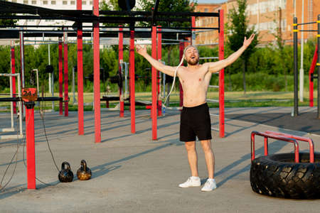 In the morning at sunrise, a man with an interesting braid hairstyle poses like a bodybuilder with a...