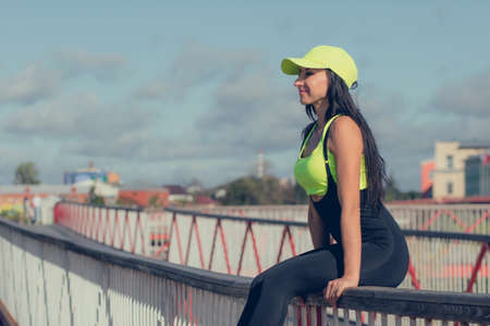 A young woman with dark hair in tight-fitting sportswear sits on a bridge.の写真素材