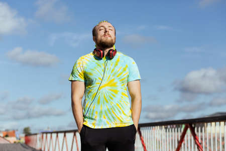 A man with an interesting mohawk hairstyle stands on the bridge wearing headphones around his neck