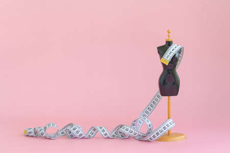 A scaled-down mannequin on a pink background with a measuring tape.