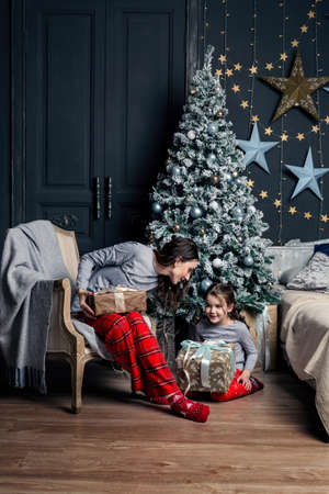 Mom and daughter in pajamas unpack New Year's gifts under the Christmas tree.の写真素材
