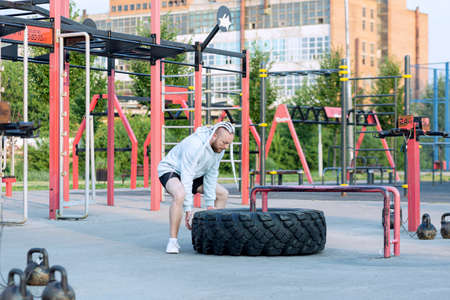 A man with a beard and interesting hairstyle does the tire press exercise (edging a heavy big tire).の写真素材