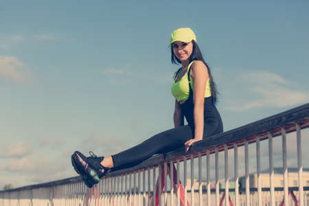 A young woman with dark hair in tight-fitting sportswear sits on a bridge.の写真素材