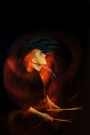 Handsome man with interesting braids on a black background with drumsticks, shot with mixed light.