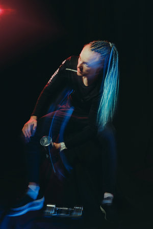 A handsome man with an interesting hairstyle from braids on a black background shakes his biceps...