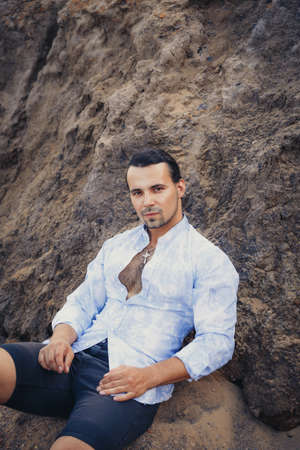 A man with dark long hair sits on a sandbank.の写真素材