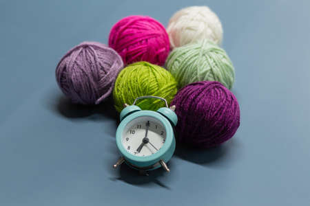 Alarm clock next to balls of wool on a blue background. Time to knit.