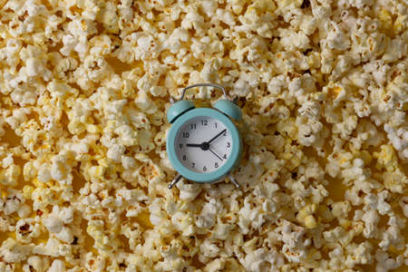 A green alarm clock lies on a background of popcorn. Time to watch a movie.の写真素材