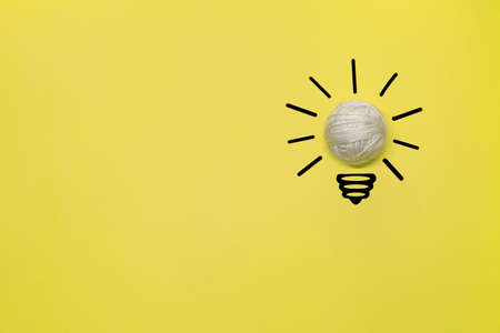 Creative thinking ideas and innovation concept. A ball of white threads with a light bulb symbol on a yellow backgroundの写真素材