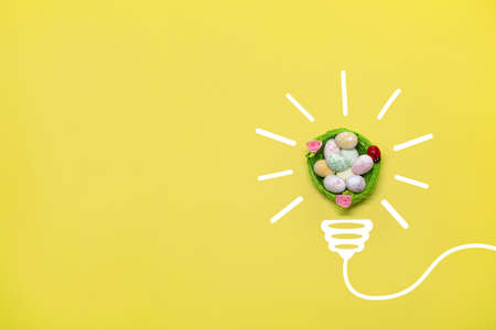 Idea symbol in the form of a painted light bulb with decorative Easter basket with eggs inside on a yellow background. Easter timeの写真素材