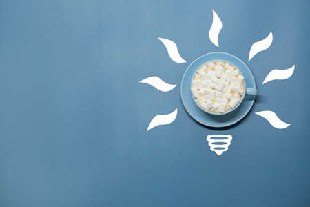 Idea symbol in the form of a painted light bulb with cup of coffee with marshmallow inside on a blue...