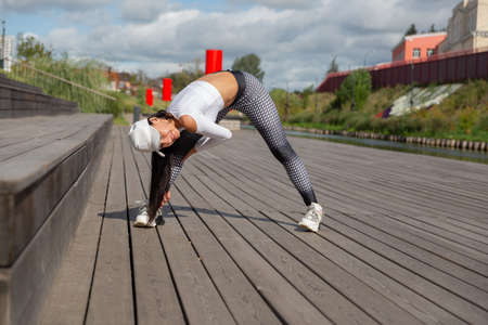 A woman in sportswear doing stretching on the river bank.