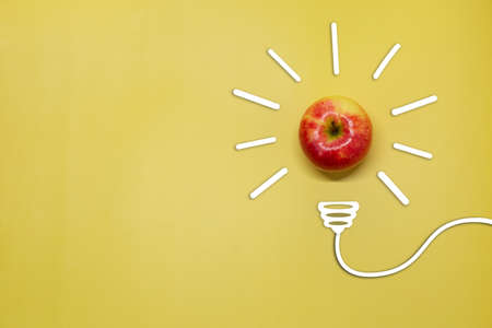 Creative thinking ideas and innovation concept. A ball of apple with a light bulb symbol on a yellow background. Time for a healthy diet.の写真素材